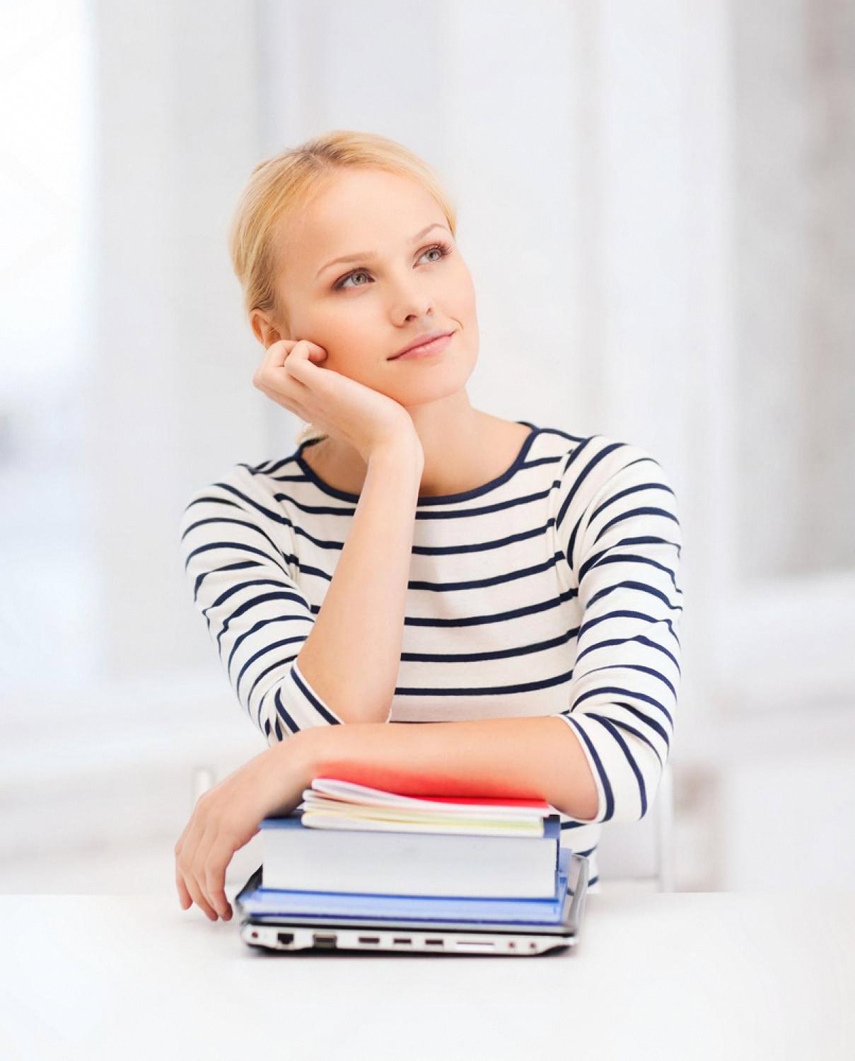 Woman in her thirties thinking about study options with books and a laptop